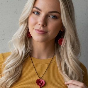 May include: A red pendant necklace and matching earrings. The pendant is heart-shaped and hangs from a dark chain. The earrings are also heart-shaped. The woman is wearing a mustard yellow crop top.