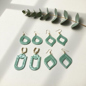 Può includere: Otto paia di orecchini fatti a mano color turchese, con varie forme, tra cui gocce e diamanti aperti. Gli orecchini hanno ganci dorati e una finitura maculata. Presentati su una superficie bianca.
