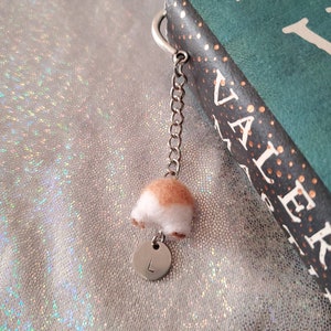 May include: A white and brown felt animal bookmark with a silver chain and a silver charm with the letter L on it. The bookmark is attached to a book with the title "VALERIE"