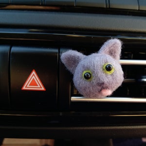 Könnte beinhalten: Ein lilafarbener Filz-Katzenkopf-Lufterfrischer für das Auto mit grünen Augen und einer heraussteckenden rosa Zunge.