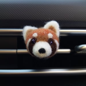 May include: A red panda plush car air freshener. The plush is made of felt and has a white face with black eyes and a black nose.