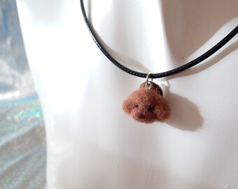 May include: A necklace featuring a brown needle-felted poodle head charm suspended from a simple black cord. The small, textured dog head has dark eyes and a dark nose, attached to the cord with a small silver-toned metal jump ring.