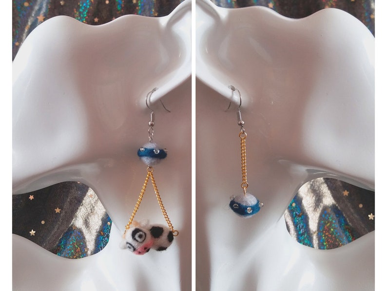 May include: A pair of dangle earrings with a blue and white felt ball charm and a gold chain. The charm has a silver ring around it with rhinestones.