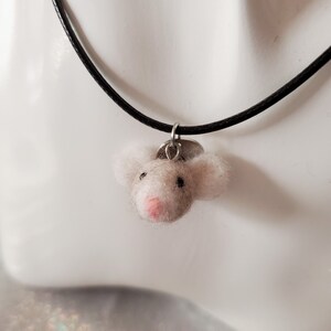 May include: A white felt mouse charm on a black cord necklace. The mouse has a pink nose and black eyes.