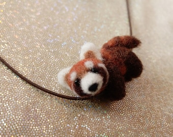 May include: A needle-felted red panda pendant attached to a thin brown cord. The red panda figure features a mix of rust-orange, dark brown, and white wool fibres, with small black eyes and a black nose, crafted in a realistic, textured style.
