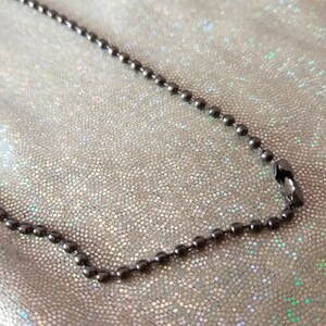 May include: A dark metallic ball chain necklace featuring a series of small, uniform spherical beads connected by short metal links. The chain includes a standard connector clasp that joins the two ends to form a continuous loop.