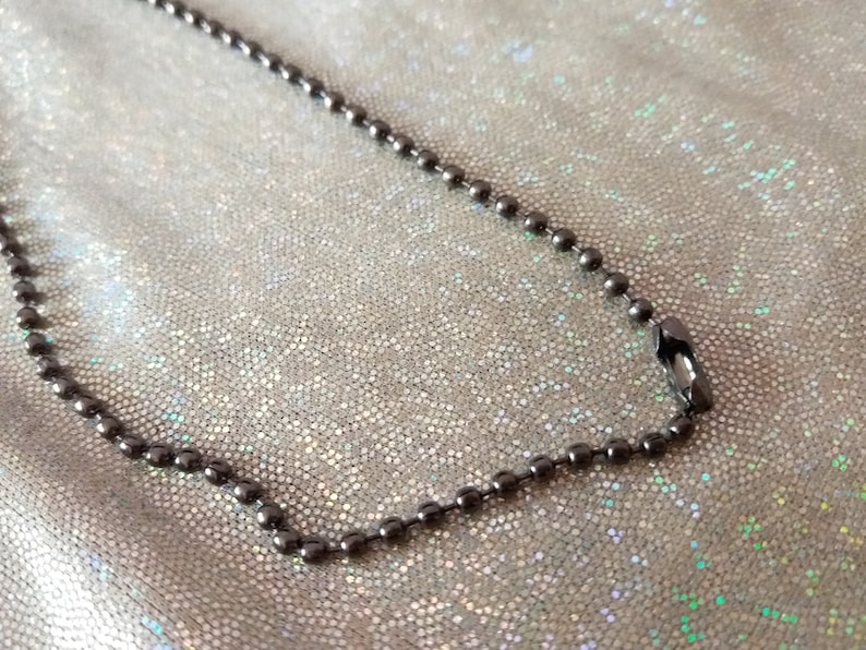 May include: A dark metallic ball chain necklace featuring a series of small, uniform spherical beads connected by short metal links. The chain includes a standard connector clasp that joins the two ends to form a continuous loop.