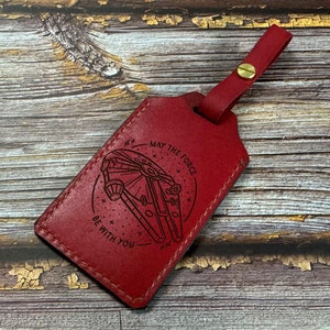 May include: Red leather luggage tag with a laser engraved design of the Millennium Falcon from Star Wars. The tag has the text "May the Force be with you".