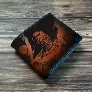 Puede incluir: Una cartera de cuero marrón con una ilustración en blanco y negro de una persona con casco y sosteniendo un arma. La cartera tiene un borde azul.