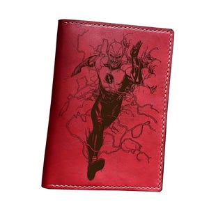 May include: Red leather wallet featuring an engraved image of The Flash in action. The wallet has a stitched border and a smooth finish. The Flash is depicted in a dynamic pose with lightning effects, a classic comic book style.