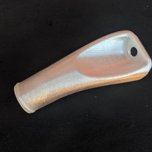 May include: A silver-coloured, elongated object with a rounded base and a flared, flattened top. The top has a small, circular hole. The object appears to be made of a textured material, possibly metal or plastic.