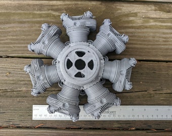 Puede incluir: Un modelo de motor radial gris impreso en 3D. El motor tiene siete cilindros dispuestos en un patrón circular alrededor de un cubo central. Se coloca una regla junto al motor para la escala, midiendo aproximadamente 25 cm de diámetro. El modelo es detallado e intrincado.