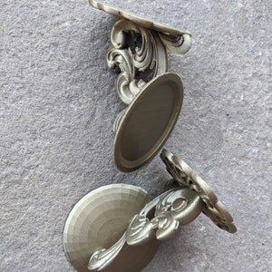 May include: Three ornate, gold-colored decorative wall shelves. Each shelf features a circular base, a decorative floral design, and a curved top. The shelves are arranged on a textured gray surface.