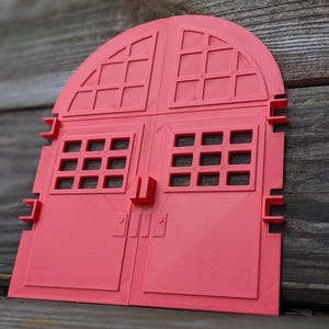 Puede incluir: Una puerta arqueada de color coral con cristales rectangulares y un tirador cuadrado. La puerta está hecha de un material sólido y tiene un diseño detallado. La puerta es probablemente un artículo decorativo o un modelo.