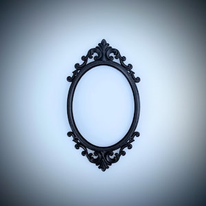 May include: Ornate black oval picture frame with decorative scrollwork. The frame has a detailed, vintage design and is centered against a white background. The frame is empty, ready for a photo or artwork.