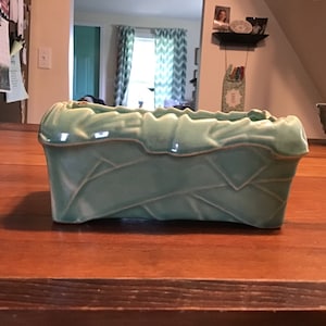 May include: A light blue ceramic planter with a geometric design. The planter is rectangular and has a slightly raised rim.