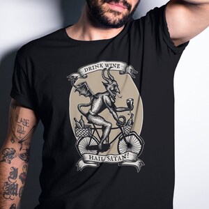 May include: Black t-shirt with a graphic of a devil riding a bicycle and holding a glass of wine. The graphic is surrounded by a banner that reads "Drink Wine Hail Satan!"