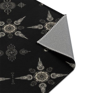 May include: Black and white patterned rug with a geometric design featuring a repeating pattern of stylized birds and celestial symbols. The rug has a gray backing and is stitched around the edges.