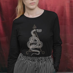 Könnte beinhalten: Ein schwarzes Langarmshirt mit einem grafischen Druck eines Schlangen, die sich um ein Dreieck mit einem Pentagramm an der Spitze windet. Die Schlange ist hellbraun und der Hintergrund des Shirts ist schwarz.