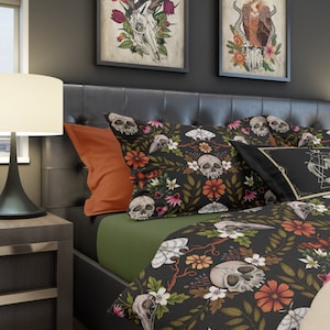 Può includere: Un set di biancheria da letto nero e verde con un motivo floreale che presenta teschi e falene. Il set di biancheria da letto comprende un copripiumino, due federe e un cuscino con un design geometrico.