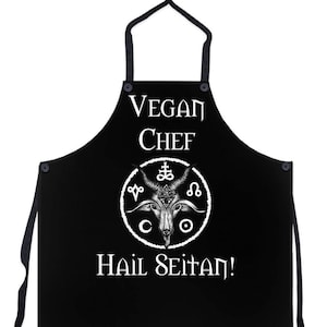 May include: Black apron with white text that reads "Vegan Chef" and a pentagram with a goat's head in the center. The text "Hail Seitan!" is below the pentagram.