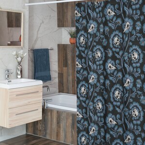 Puede incluir: Una cortina de ducha negra con un patr&oacute;n floral azul con dise&ntilde;os de calaveras blancas. La cortina de ducha est&aacute; colgada en un ba&ntilde;o con una ba&ntilde;era blanca y azulejos de imitaci&oacute;n de madera.