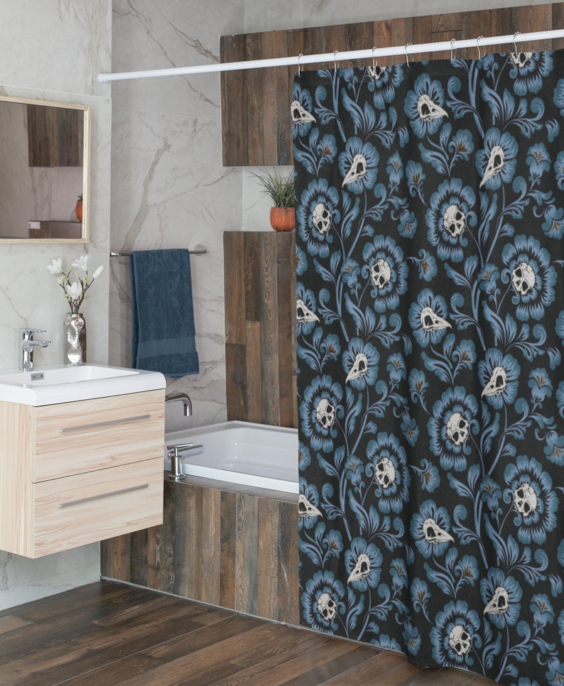 Puede incluir: Una cortina de ducha negra con un patr&oacute;n floral azul con dise&ntilde;os de calaveras blancas. La cortina de ducha est&aacute; colgada en un ba&ntilde;o con una ba&ntilde;era blanca y azulejos de imitaci&oacute;n de madera.