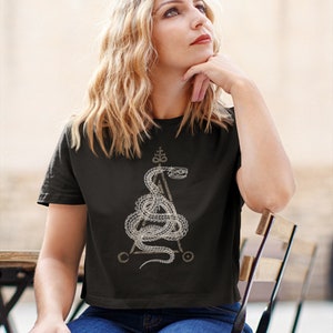 May include: A black cropped t-shirt with a white graphic of a snake wrapped around a triangle with a symbol at the top. The snake is stylized and has a detailed design.