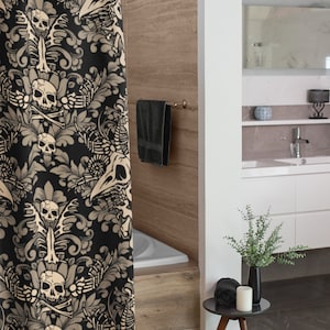 Op de afbeelding: Een zwarte douchegordijn met een beige bloemenpatroon met schedels en botten. Het gordijn hangt in een badkamer met een wit bad en een houten vloer.