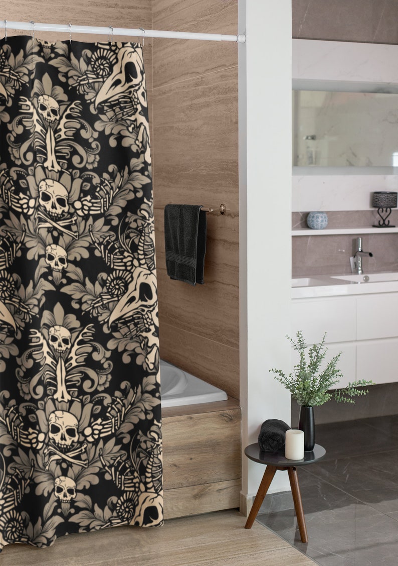 Op de afbeelding: Een zwarte douchegordijn met een beige bloemenpatroon met schedels en botten. Het gordijn hangt in een badkamer met een wit bad en een houten vloer.