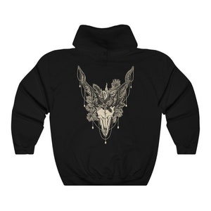 May include: Black hooded sweatshirt featuring a detailed cream-colored illustration of a skull adorned with floral and beaded accents. The design is centered on the back of the sweatshirt, creating a striking visual.