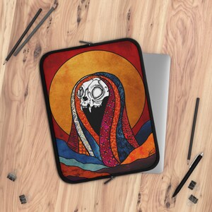 May include: A laptop sleeve with a colorful, patterned design featuring a skull with a large, open mouth. The skull is surrounded by a colorful, patterned scarf. The background is a sunset with a yellow sun and red and orange clouds.