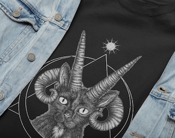 Pode incluir: Camiseta preta com uma ilustração detalhada de um gato com chifres de cabra, inserida em um pentagrama e formas geométricas. Um símbolo semelhante ao sol está acima do gato. A camiseta é emoldurada por uma jaqueta jeans azul clara.