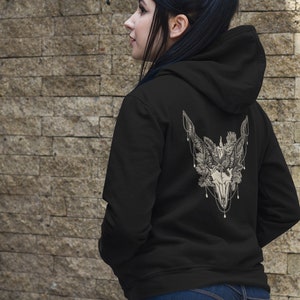 May include: Black hoodie with a detailed white graphic on the back featuring a skull, feathers, and floral elements. The design is intricate and centered on the upper back of the hoodie. The hoodie has a hood and a simple, classic design.
