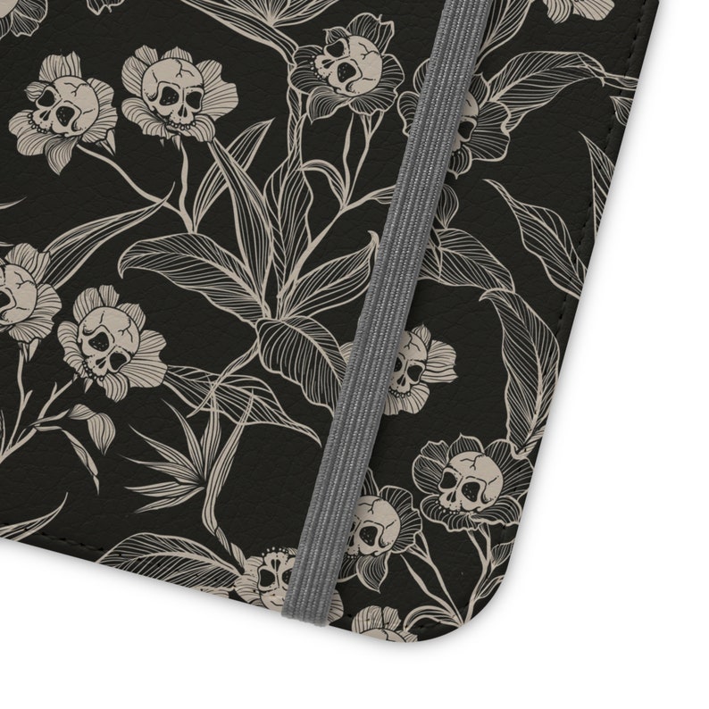 May include: Black leather notebook cover with a white floral pattern featuring skulls. The cover has a grey elastic closure.