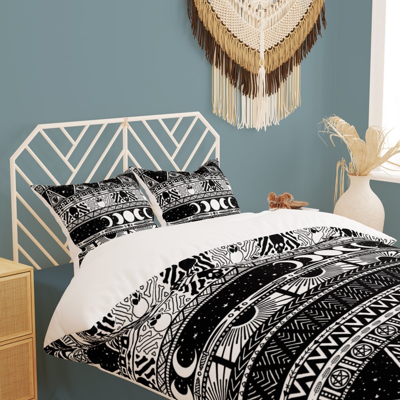 May include: Black and white duvet cover with a geometric pattern featuring moons, stars, and other celestial symbols. The duvet cover is on a bed with white pillowcases and a white headboard.