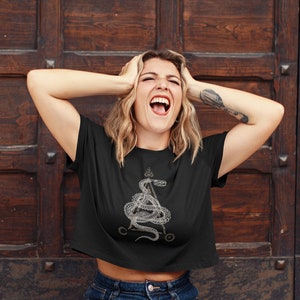 May include: A black cropped t-shirt with a white graphic of a snake wrapped around a pentagram. The snake has a crown on its head.
