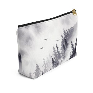 May include: A white zippered pouch with a black and gray watercolor design of a forest with trees and birds. The pouch is made of canvas and has a zipper closure.