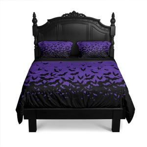 May include: A black bed frame with a headboard and bedding set. The bedding features a purple and black bat pattern on the duvet cover and pillowcases. The headboard is ornate and the bed is against a white background.