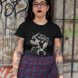 Może przedstawiać: Czarny t-shirt z grafiką modlącej się modliszki i tekstem "Eat the Patriarchy" z symbolem żeńskim.