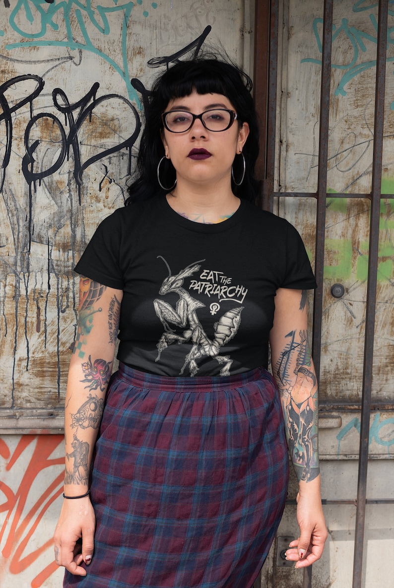 Może przedstawiać: Czarny t-shirt z grafiką modlącej się modliszki i tekstem "Eat the Patriarchy" z symbolem żeńskim.