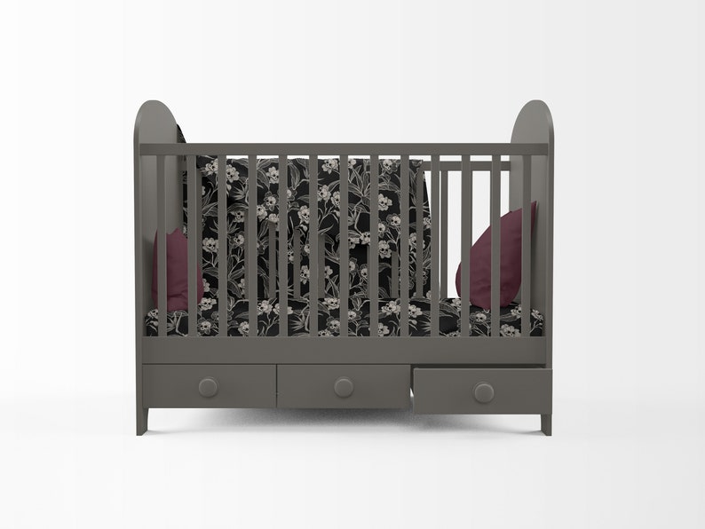 May include: A gray crib with a black and white floral print bedding set and two burgundy pillows. The crib has three drawers underneath.