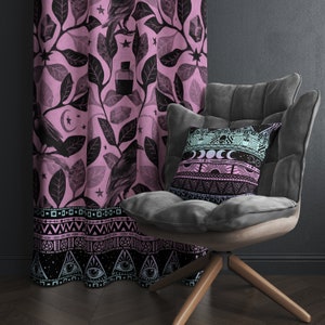 May include: A black armchair with a pink and black patterned throw pillow. The pillow has a celestial design with moons, stars, and a sun. The armchair is in front of a pink curtain with a black floral pattern and a black crow design.