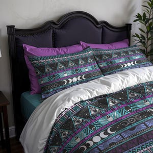 Op de afbeelding: Een bed met een zwart hoofdbord en paarse kussens. Het beddengoed heeft een zwart, blauwgroen en paars patroon met ogen, manen en geometrische vormen. Het dekbedovertrek is wit.