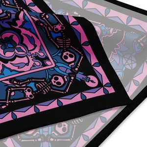 Puede incluir: Un pañuelo de tela negro con un diseño de vidriera rosa y azul con esqueletos y velas. El diseño es intrincado y detallado, con una estética gótica.