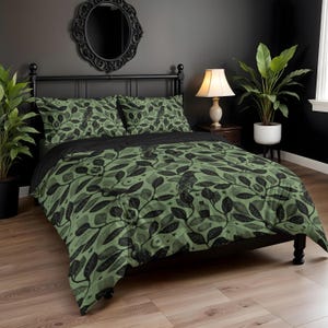 Könnte beinhalten: Ein Bett mit schwarzem Metallrahmen und einer grün-schwarzen Bettdecke und Kissenbezügen mit Blättermuster. Die Bettwäsche hat ein botanisches Design mit Sternen und einem Raben. Ein schwarzer Bettrand und ein schwarzer Spiegel sind ebenfalls sichtbar.