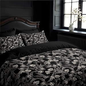 May include: Black and white bedding set with a floral pattern featuring skulls. The bedding is on a bed with a dark headboard and black pillows.