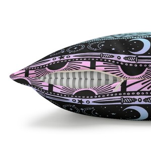 May include: A black pillow with a zipper closure. The pillow has a repeating pattern of moons, stars, suns, and daggers in pink, blue, and white on a black background.