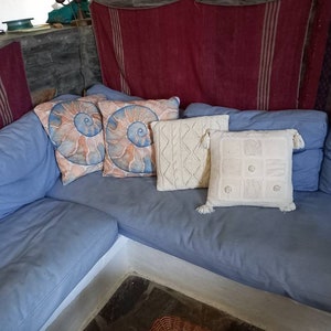 May include: A blue sectional sofa with a variety of throw pillows. The pillows are decorated with a seashell pattern, a white knit pattern, and a white geometric pattern.