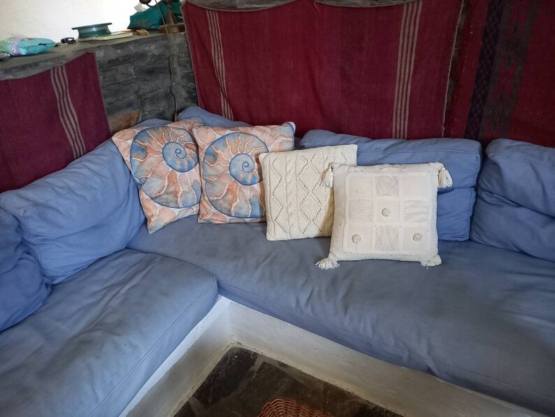 May include: A blue sectional sofa with a variety of throw pillows. The pillows are decorated with a seashell pattern, a white knit pattern, and a white geometric pattern.